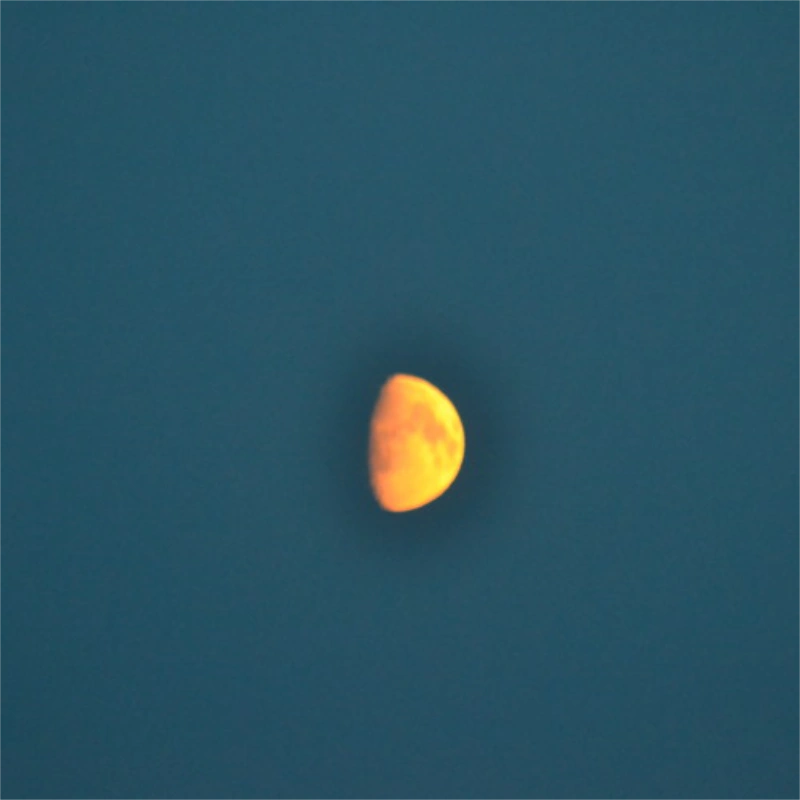 Close-up of a blurred, orange-tinted half moon against a deep blue sky at dusk.