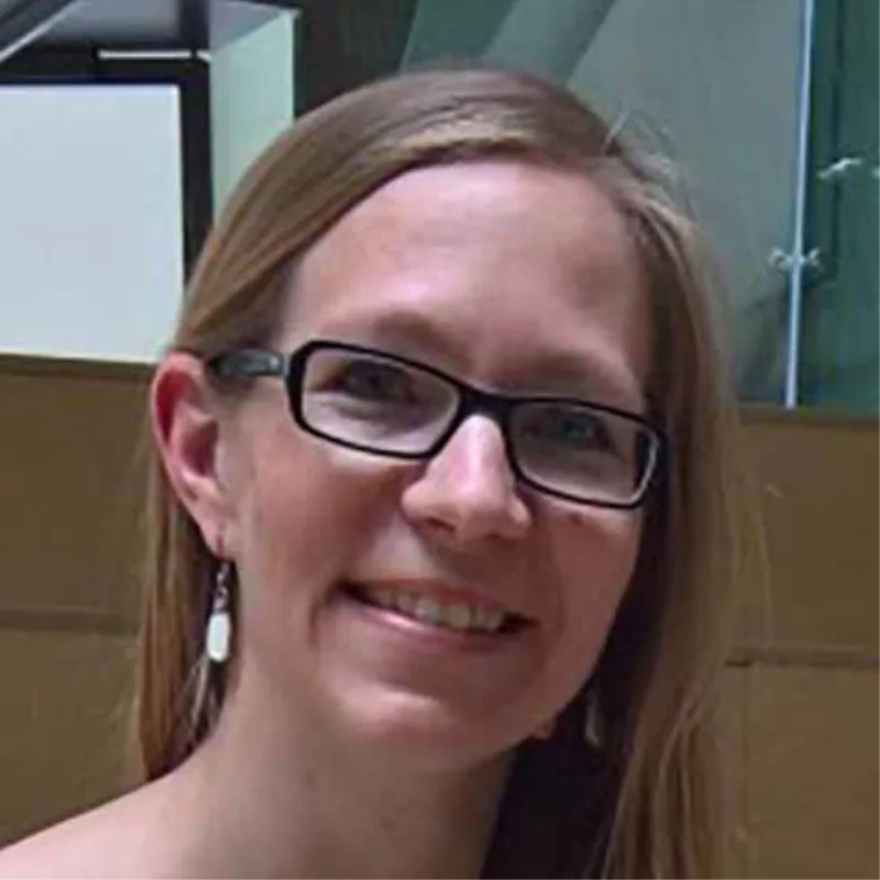 En kvinde med langt hår og briller, der smiler foran en uskarp baggrund.