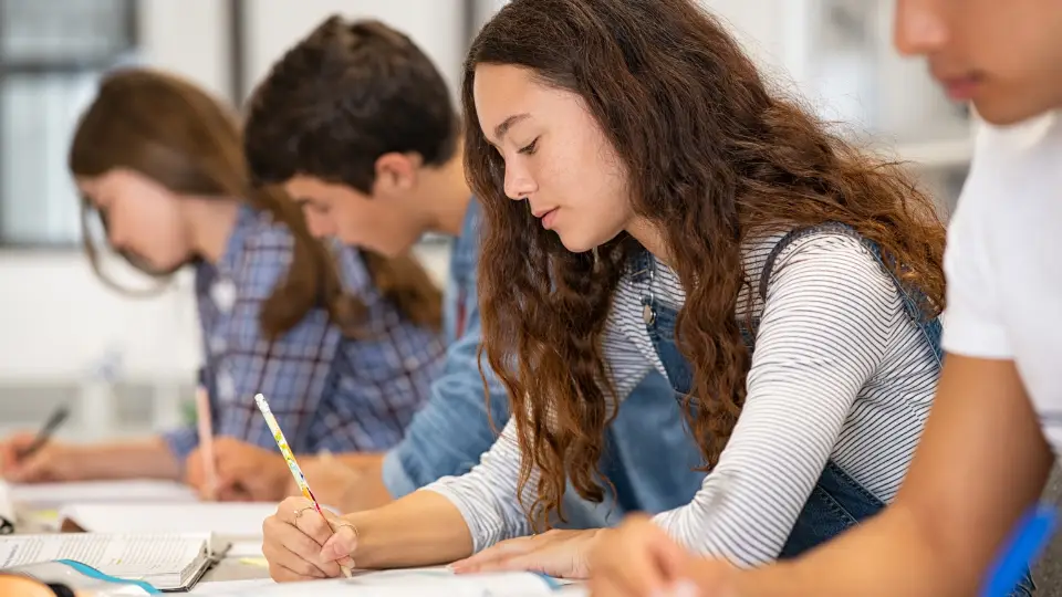 Ungdommer som sitter på rad ved pultene og skriver i et klasserom.