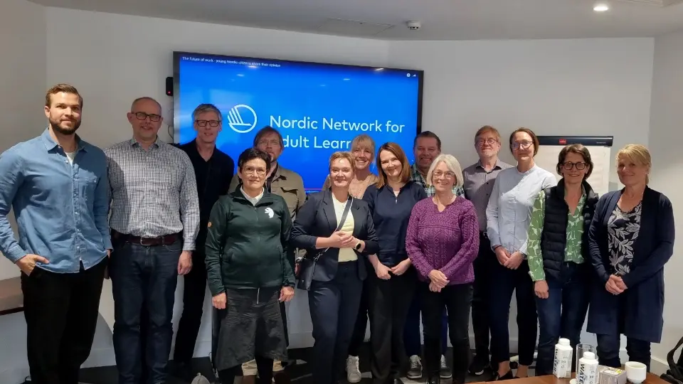 En grupp av elva personer står framför en skärm med texten "Nordic Network for Adult Learning" i ett konferensrum.