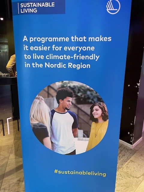 Blue banner promoting a Nordic climate-friendly living program, with a circular photo of three young people talking, accompanied by the hashtag #sustainableliving.